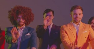 Group of funny happy dancer men and women wearing suits dancing together celebrating success at corporate party indoors. Coworkers or young friends having fun in neon lights. 4k video.