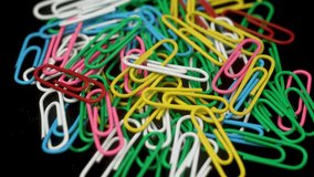 Multicolored rotating paper clips. Macro stationery supplies. Colorful paper clips on black desk, close up