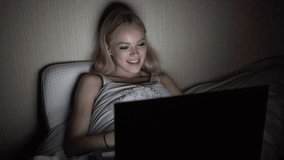 A woman watches a movie at night in bed and yawns.