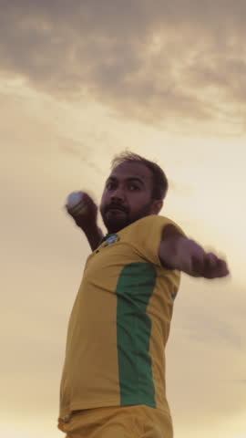 Vertical Screen: Portrait of a South Asian Cricket Player in Yellow and Green Uniform Throwing the Ball on a Pitch. Professional Indian Bowler is Focused, Aiming to Hit the Wicket With His Shot