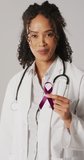 Vertical video of happy biracial female doctor holding purple ribbon. health, medicine, prevention and cancer awareness concept.