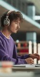 Vertical Screen: Handsome European Student Studying in a Traditional Library. Young Male Wearing Headphones, Working on an University Research Project, Reading Academic Textbook and Journals Online