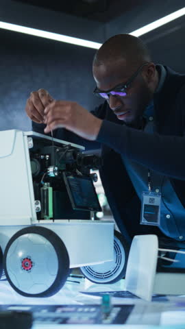 Vertical Screen: Close Up of an Engineer Using a Screwdriver While Developing a Remotely Controlled Delivery Robot. Black Specialist Working in High Tech Research Laboratory with Modern Equipment