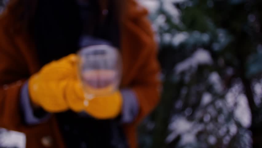 A traveler in a brown coat holds a thermos in a winter forest. Hiker exploring woods, festive Christmas atmosphere. Woman enjoying outdoor adventure.	