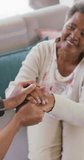 Vertical video of senior african american woman holding hands with female physiotherapist at home. senior healthcare and medical physiotherapy treatment.