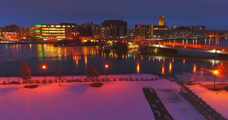 Winter nighttime twilight view of Green Bay Wisconsin Downtown with glowing city lights, snow, and icy Fox River.