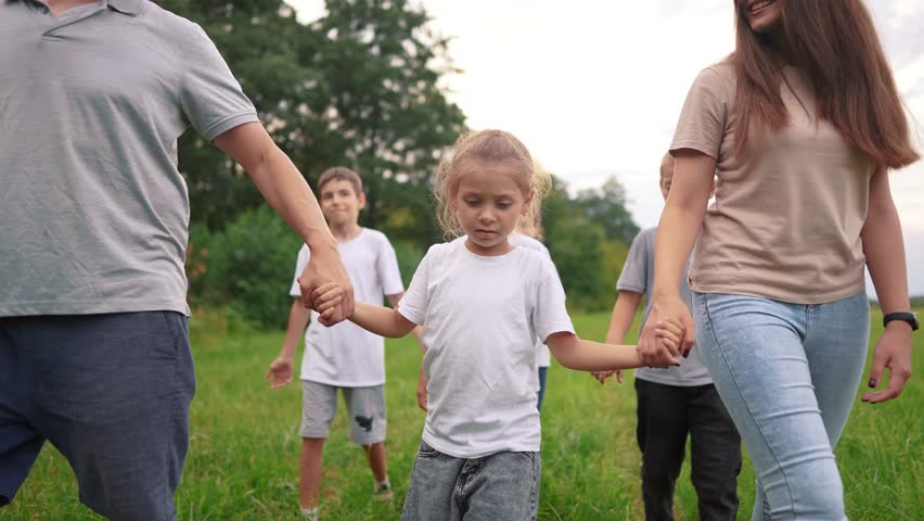 family walking on the grass in the park and holding hands. happy family childhood dream concept. a large family lifestyle walks across the clearing and talks to each other. outdoor nature walk