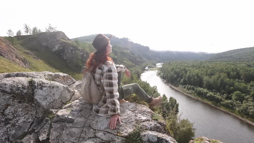 A beautiful young girl with a backpack and a hat is enjoying a sunny day at the top of the mountain. A tourist is a traveler on the background of the layout of the valley landscape. Hiking on the Sham