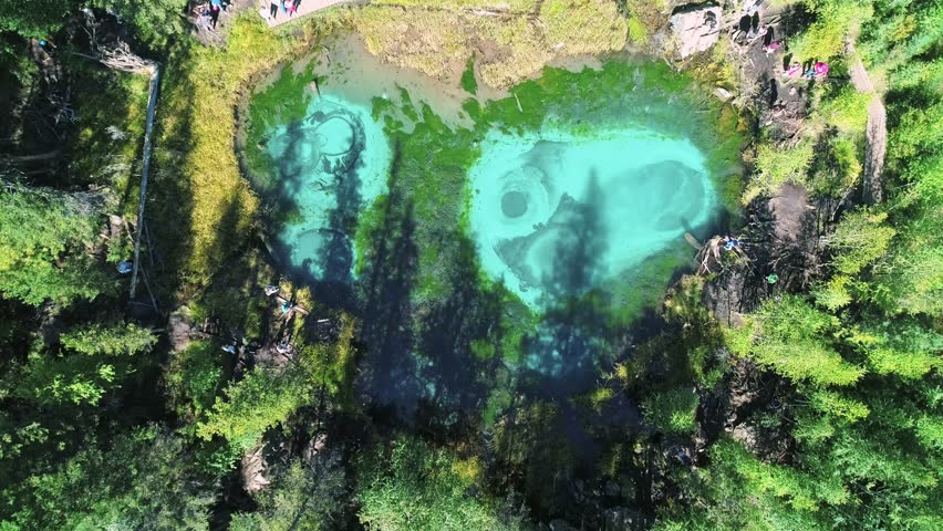 Aerial over the turquoise geyser lake with transparent mineral water and blue clay on the lakebed. Lake surrounded with green forest. Beauty in nature