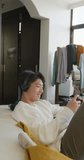 Vertical video of asian male teenager playing video games in living room. spending time alone at home.
