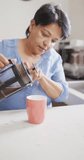 Vertical video of senior biracial woman with blue shirt preparing coffee in kitchen. healthy and active retirement at home.