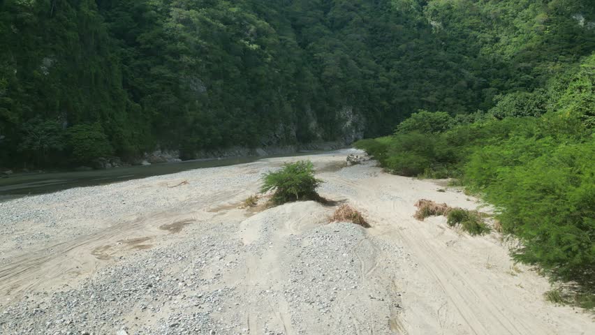 Aerial forward at low altitude over riverbank at Muchas Aguas with people in background, Dominican Republic
