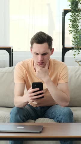 Distressed man sitting with phone on sofa at home Royalty-Free Stock Footage #3454929757