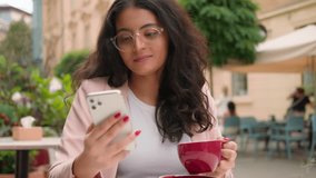 Close up thoughtful Indian Arabian woman ethnic female girl businesswoman tourist using looking mobile phone scrolling smartphone reading news social media holding coffee cup city street cafe outside - Powered by Shutterstock - Get 15% off with code: PIKWIZARD15