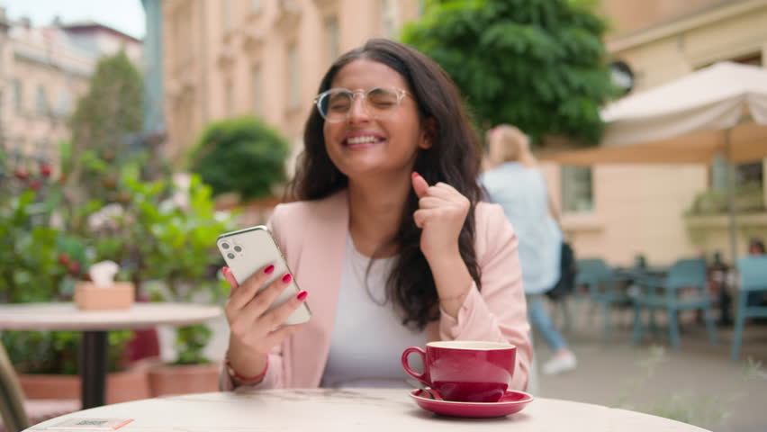 Happy joyful smiling Indian Arabian ethnic woman female girl receive positive message notification mobile phone celebrating victory. Winning shock smile laugh outside city street cafe online business Royalty-Free Stock Footage #3454936963