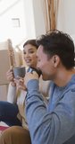 Vertical video of happy asian couple drinking coffee in new house. lifestyle, moving and owning new house concept