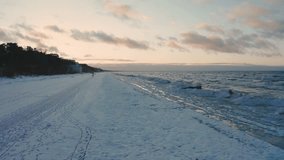 Drone view above Jurmala marine beach presents somber scene in midst of winter. Aerial view winter Baltic sea ice sunset waves. Drone vertical video of beautiful beach located at famous Latvian resort