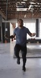 Vertical video of fit african american man jumping on jumping rope at gym. active, fit, sporty and healthy lifestyle, exercising at gym concept.