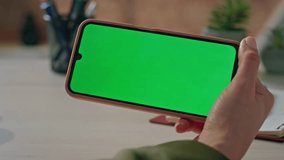 Woman touching green screen mobile phone in horizontal position at workplace closeup. Unrecognizable girl swiping mockup smartphone watching video. Female finger tapping chroma key cellphone in office