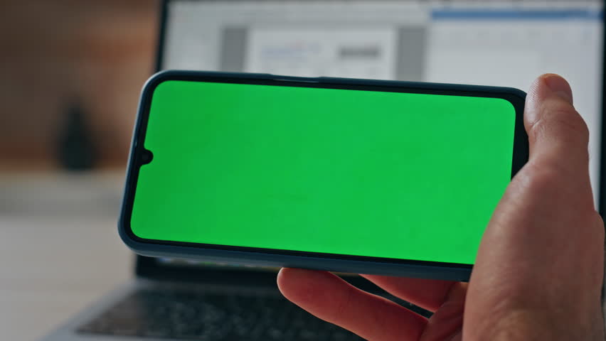 Man hands hold chromakey phone in office closeup. Unrecognizable businessman reading news on green screen device zoom out. Unknown boss listening virtual call visiting online meeting at laptop table  Royalty-Free Stock Footage #3455004515