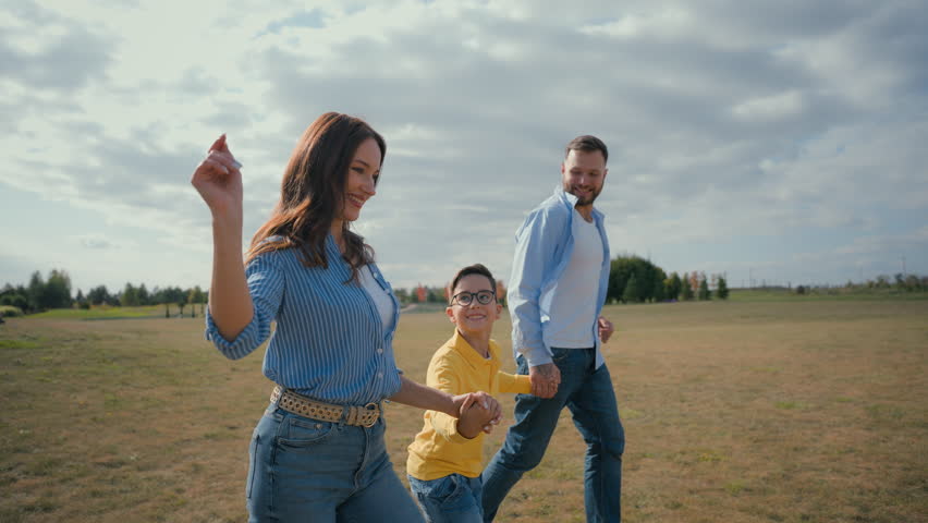 Happy European family smiling laughing man woman couple little boy son kid running outside nature countryside meadow mom dad child holding hand run rural field happiness joy parenting custody adoption Royalty-Free Stock Footage #3455006299