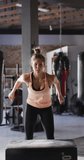 Vertical video of fit caucasian woman jumping on block at gym. active, fit, sporty and healthy lifestyle, exercising at gym concept.