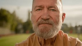Close up old Caucasian man pensioner looking at camera serious face expression calm silently blinking athlete recreation stadium outside city relax sportsman bearded wrinkled male wellbeing lifestyle - Powered by Shutterstock - Get 15% off with code: PIKWIZARD15