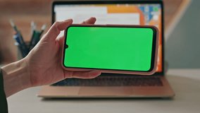 Unknown student browsing mockup mobile phone at office desk close up. Woman hands tapping at green screen smartphone turning on online video. Businesswoman having video call by chroma key cellphone.
