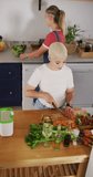 Vertical video of happy biracial woman cutting vegetables in kitchen. spending quality time at home.