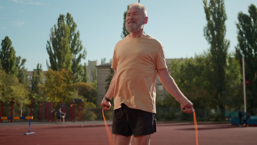 Old Caucasian man jumping rope athlete smiling stadium city outside sport physical activity elderly sportsman workout training wellbeing strong fitness healthcare lifestyle muscular exercise endurance - Powered by Shutterstock - Get 15% off with code: PIKWIZARD15