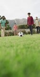 Vertical video of happy diverse male friends playing football in garden. healthy and active time holiday.