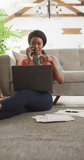 Vertical video of african american woman sitting on floor and using laptop. home office and online working concept.