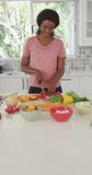 Vertical video of happy african american woman preparing meal in kitchen. cooking, lifestyle and spending time at home.