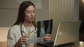 A medical professional, presumably a doctor, is engaged in a virtual consultation. She is holding a radiograph up to the camera for closer examination while explaining its details. The setting appears