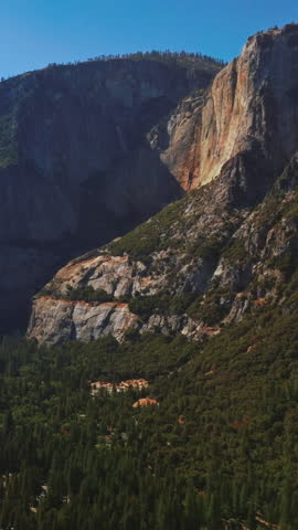 Amazing steep mountains in Yosemite National Park, California, USA. Beautiful sunny valley with green pine tree wood. Aerial view. Vertical video.