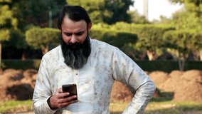 Beard men of Indian ethnicity wearing traditional clothing (kurta-Pajama) standing outdoor in nature and talking on mobile phone.