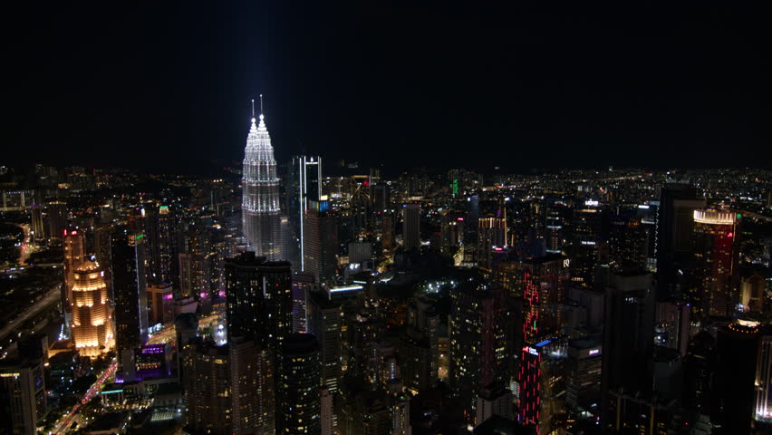 vibrant night scene of Kuala Lumpur, highlighting the brightly lit Petronas Towers amid a sprawling urban landscape