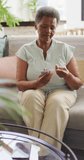 Vertical video of senior african american woman using glucose meter at home. senior healthcare and medical physiotherapy treatment.