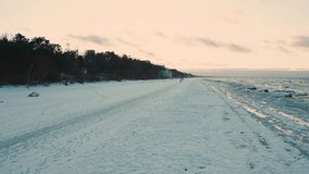 Drone view above Jurmala marine beach presents somber scene in midst of winter. Aerial view winter Baltic sea ice sunset waves. Drone vertical video of beautiful beach located at famous Latvian resort