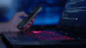 Cybercriminal sitting in front of laptop doing something with smartphone - Powered by Shutterstock - Get 15% off with code: PIKWIZARD15