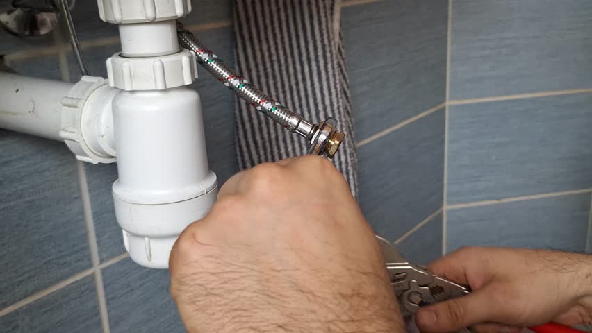 The plumber removes the end cap from the water supply hose. The plumber's hands remove the blanking plug from the metal braided hose. Concept of small repairs in home, housekeeping, DIY, maintenance Royalty-Free Stock Footage #3455414155