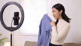 Young woman at home is doing extra work at home by selling clothes online. She is live-streaming her online sales on social media.