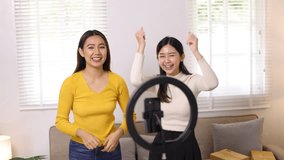 Two young influencer Asian woman dance while live-streaming an online sales event on social media from home.
