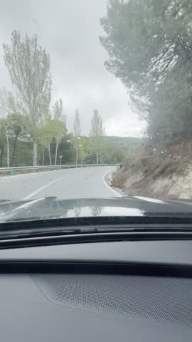 First person view, FPV, from dashcam of car driving in the Sierra Nevada mountains, Granada, Andalusia, Spain, Europe, in the rain. Road trip vertical video in POV from inside vehicle