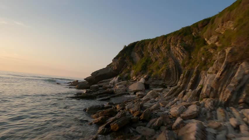 Drone flying at low altitude along rocky cliff at sunset, Hendaye, Pyrenees Atlantiques, France. Aerial FPV