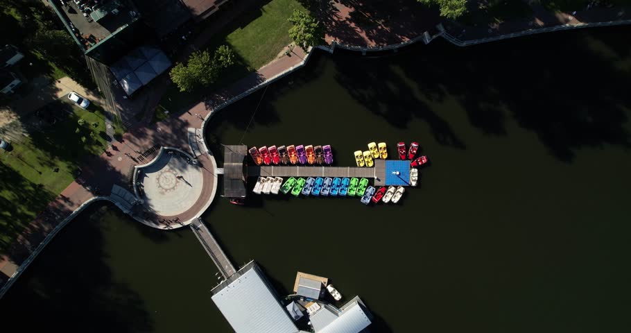 Colorful boats and catamarans for walking in the pond are moored on the pier, aerial shot. Rental of catamaran boats for walks on the lake. Top view