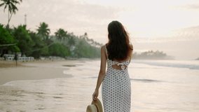 Pretty smiling girl in dress turns around, walks at ocean shore, sea surf at sunrise. Young caucasian woman going along empty seaside, tropical plants in the morning. Happy lady relaxing at vacation. - Powered by Shutterstock - Get 15% off with code: PIKWIZARD15