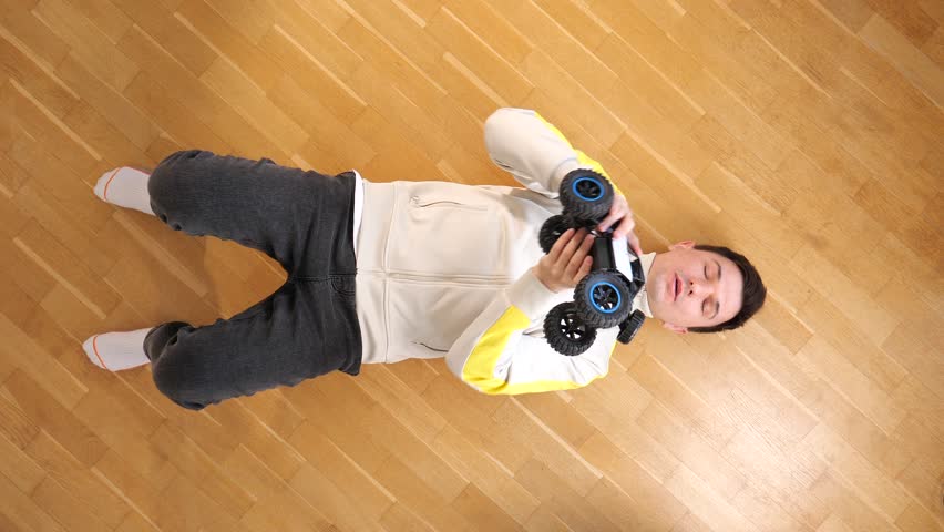 top view of a man lying on floor and throwing up model of a rc car toy truck