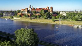 Royal Wawel Cathedral and castle in Krakow, Poland. Aerial 4K approaching video in sunset light. Vistula River, canoes, tourist boat,  riverbank with park, promenade and walking people and bikers