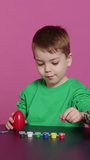 Vertical Video Young toddler focusing on decorating easter eggs with stamps and watercolor paint, preparing handcrafted ornaments for spring holiday festivity. Small cute boy coloring decorations